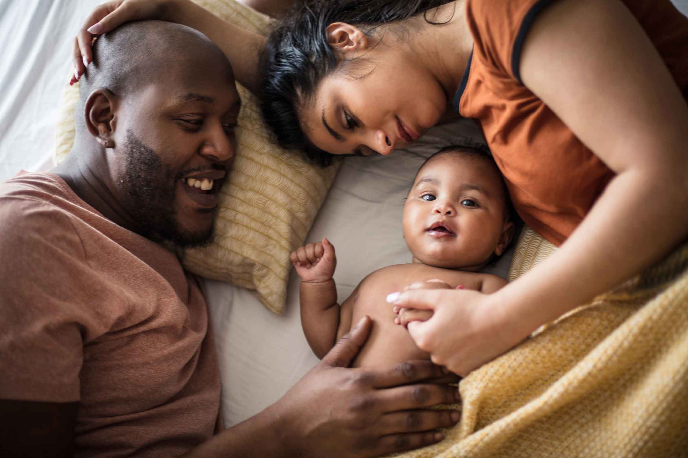 woman and man laying on a bed holding a baby